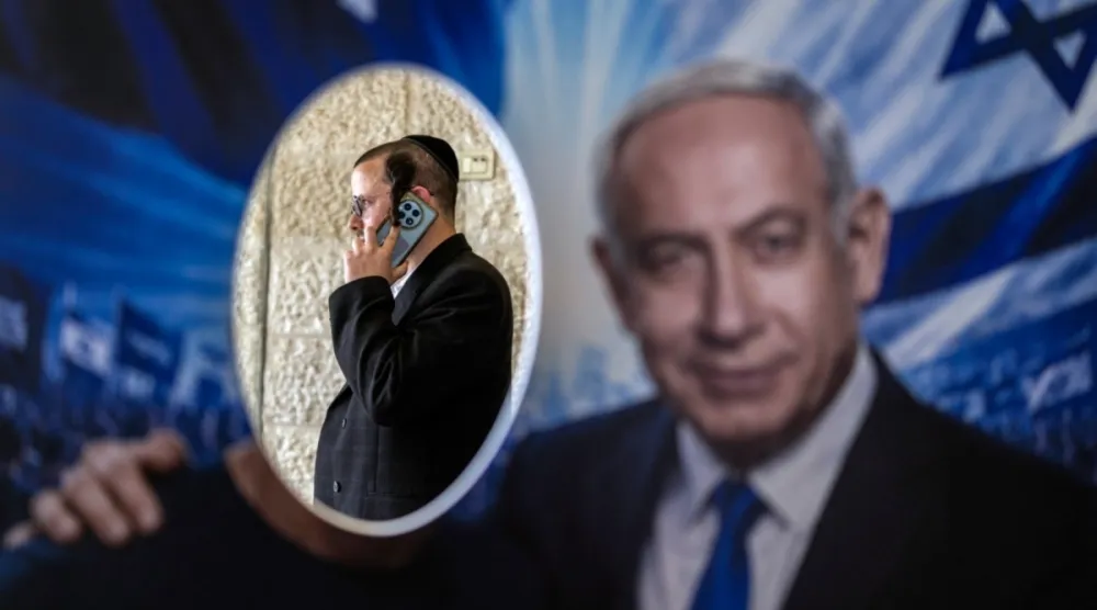 Kudüs'te, İsrail seçimlerinden önce parti ön seçimleri sırasında bir seçim merkezinde, Likud partisi üyesi, İsrail Başbakanı Binyamin Netanyahu'ya ait bir posterin arkasında duruyor(AFP)