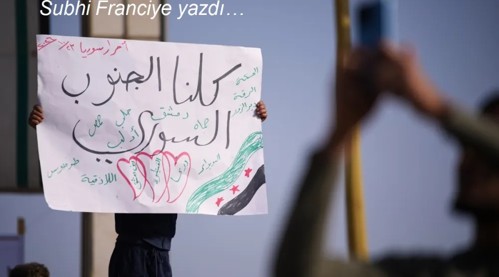 Suriye'nin Dera şehrinde, Kuneytra ve batı Dera bölgelerine yönelik İsrail askeri müdahalelerine karşı düzenlenen protestoda, bir gösterici Arapça olarak “Hepimiz Güney Suriye'yiz” yazılı pankart taşıyor, 23 Ekim 2026