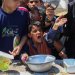 صبي فلسطيني مع أقرانه يحاول الحصول على الطعام من مطبخ خيري في مخيم النصيرات وسط غزة يوم الاثنين (أ.ف.ب)
