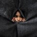 طفل فلسطيني نازح ينظر من خلال غطاء مصنوع من البطانيات أثناء لجوئه إلى مدرسة تديرها «الأونروا» في خان يونس جنوب قطاع غزة (رويترز)