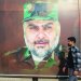 عراقي بأحد شوارع بغداد يمر أمام صورة لمقتدى الصدر مرتدياً الزي العسكري الخاص بـ«سرايا السلام» (أ.ف.ب)