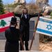 إسرائيلي متشدد يلتقط صورة قرب عَلَمَي لبنان وإسرائيل مرفوعين على نصب تذكاري في بلدة المطلة المحاذية للحدود اللبنانية (أ.ب)