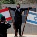 يهودي متشدد يقف بجانب العلمين الإسرائيلي واللبناني على الحدود بين البلدين (أ.ف.ب)