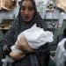 سيدة فلسطينية مصابة تحمل طفلها حديث الولادة بأحد مستشفيات غزة (رويترز)