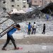 صبي فلسطيني يحمل طاولة يمر قرب عمال يجمعون أنقاض مبان دمرتها إسرائيل في الحرب على غزة (أ.ف.ب)