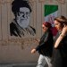 إيرانيتان تمران قرب صورة للمرشد الإيراني السابق علي خامنئي الذي قُتل في الضربات الأميركية - الإسرائيلية في 28 فبراير وأعلام إيرانية وسط طهران - 20 أغسطس 2026 (أ.ب)