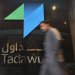 رجل يعبر أمام شعار «تداول» في السوق السعودية (رويترز)