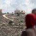 الفلسطيني محمود الطوباسي (60 عاماً) وزوجته عايدة (51 عاماً) يقفان بمنطقة تطل على منزلهما الذي تضرر جراء هجوم شنه مستوطنون إسرائيليون في جالود بالضفة الغربية المحتلة الثلاثاء (رويترز)