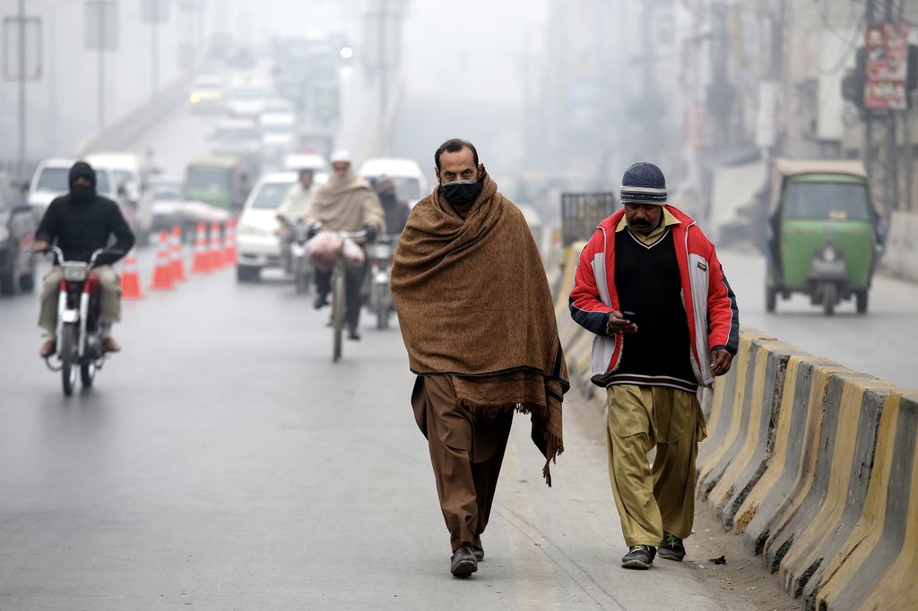رجل يرتدي شالاً تقليدياً يمشي على طول الطريق وسط ضباب كثيف في بيشاور - باكستان الخميس (إ.ب.أ)